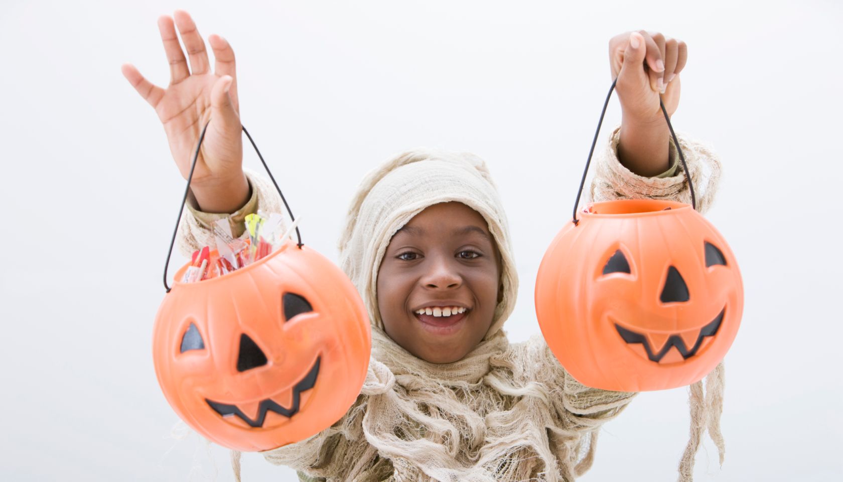 Black boy in mummy costume holding jack o'lanterns