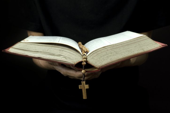 Cropped Hand Of Person Holding Rosary While Reading Bible Against Black Background