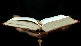 Cropped Hand Of Person Holding Rosary While Reading Bible Against Black Background