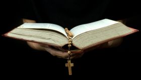 Cropped Hand Of Person Holding Rosary While Reading Bible Against Black Background