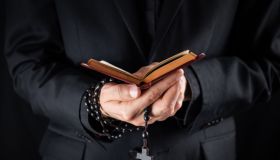 Midsection Of Priest Holding Prayer Beads And Bible While Standing Against Black Background