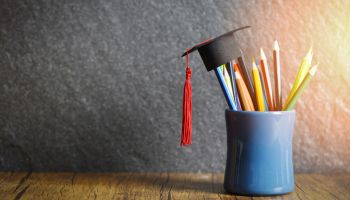 Close-Up Of Multi Colored Pencils With Mortarboard In Desk Organizer On Table